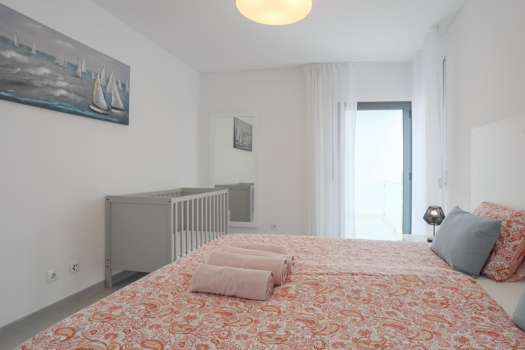 Hoofdslaapkamer met een queensize bed, een standaard kinderbedje en een eigen balkon.